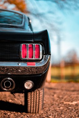 Eski bir arabanın arka stop lambası ve egzoz sisteminin detaylı bir yakın çekimi. Arkaplanı bulanık, cilalı bitiş ve klasik tasarım özellikleri sergiliyor..