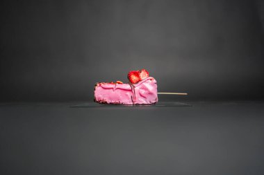 Üzerinde taze çilek dilimleri olan donmuş pembe çilekli dondurmanın yakın plan görüntüsü çarpıcı ve iştah açıcı bir sunum için minimalist koyu bir arka plana yerleştiriliyor..