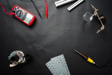 Various electronics tools and small components arranged on a black surface, including a multimeter, soldering iron, and metallic pieces, creating an organized workspace for engineering or DIY projects clipart