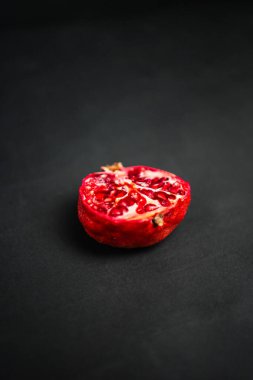 Koyu bir zemin üzerinde canlı kırmızı tohumlar sergilenen yarım nar, doğal dokusunu vurguluyor ve zıt renkleri vurguluyor, sağlıklı yemek ve sanatsal yiyecekler için mükemmel.