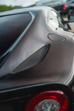 Kırmızı arka lambası ve karbon fiber takılı, modern otomotiv tasarımı sergilenen arka tarafı odaklı parlak siyah bir arabanın ayrıntılı görüntüsü.