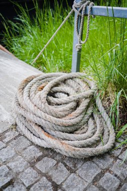 Açık hava ortamlarında gücü, doğayı ve geleneği sembolize eden yemyeşil otların yanındaki taştan yolda sarmal halatın detaylı bir görüntüsü..