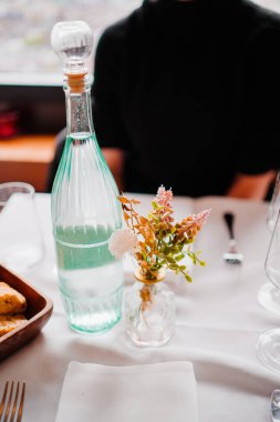 Su dolu cam bir şişe ve narin çiçeklerle dolu küçük bir vazonun yer aldığı güzel düzenlenmiş bir masa, sade ve misafirperver bir atmosfer yaratıyor..