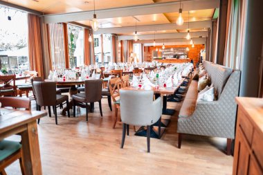 Resmi bir toplantı için süslenmiş masaları olan şık bir restoranın içi şık dekorlu ve geniş ışıklandırmalı bir ortamda rafine bir atmosfer sergiliyor..