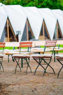 Katlanan sandalyeler mimari arkaplanlı çakıl döşemelerine yerleştirilmiş. Görüntü, kırsal bir atmosferi betimliyor. Açık hava toplantıları, etkinlikler veya düğünler için mükemmel..