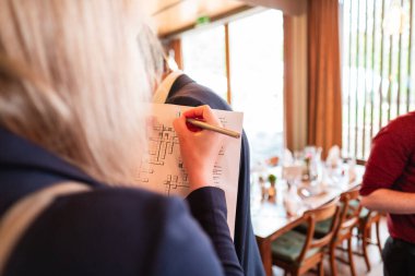 A close-up shot of a hand solving a crossword puzzle in a lively event setting with blurred dining tables and attendees in the background. clipart