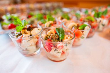 Bireysel porsiyonlu salata fincanlarının yakın plan çekimi. İçinde sebzeler, taze otlar ve fındıklar var. Bir etkinlik ya da toplanma için bir masada sergileniyor..