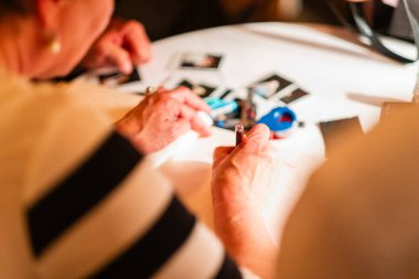 Yaratıcı malzemeler ve fotoğraflarla çevrili, odaklanma, yaratıcılık ve sanatsal bağlılığı temsil eden, iyi aydınlatılmış bir masadaki bir kağıt parçasına kalem kullanarak aktif olarak yazan eller..