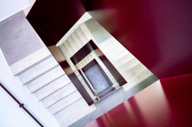 Çağdaş mekanlarda geometrik şekilleri, simetriyi ve mimari tasarımı vurgulayan, beyaz basamakları ve kırmızı duvarları olan modern spiral merdivenlerin soyut perspektifi.