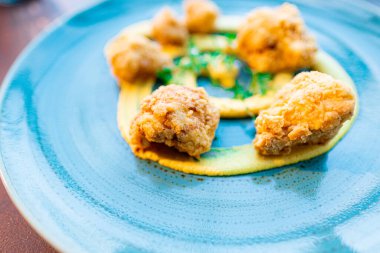 A plated dish features crispy golden fried chicken served on a blue plate, accompanied by an artistic garnish of sauce and fresh greens, creating an elegant and appetizing presentation. clipart