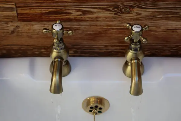 Samimi banyodaki klasik pirinç musluklar: pirinç musluklu bir kırsal banyo lavabosu. Eski tarz musluklardan birinden su akmaktadır. Pirinç ve ahşap karışımı banyoya eski moda bir cazibe katar..