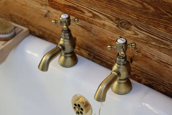 Samimi banyodaki klasik pirinç musluklar: pirinç musluklu bir kırsal banyo lavabosu. Eski tarz musluklardan birinden su akmaktadır. Pirinç ve ahşap karışımı banyoya eski moda bir cazibe katar..