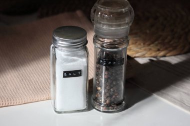 A close-up shot of a classic salt shaker and pepper grinder set. Fine white salt and whole black peppercorns. High-quality photo clipart