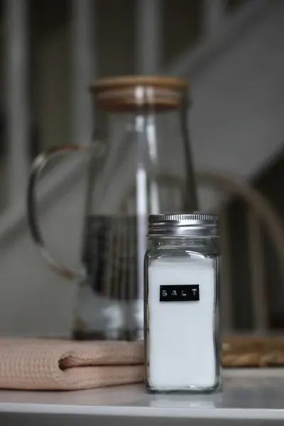Üzerinde SALT yazan metal kapaklı cam tuzluk ve ahşap kapaklı şık bir su sürahisi olan bir mutfak düzeneği. Her gün yemek ve yemek, yüksek kaliteli stok fotoğrafı.