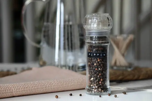Biber öğütücü, içi tamamen karabiber dolu, rahat bir mutfak masasına kurulmuş. Ev yemeği, temel baharat unsurları stok imajı. Yüksek kaliteli fotoğraf.