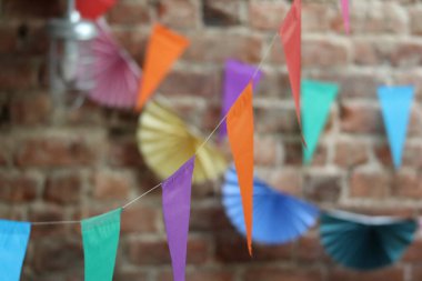 Açığa çıkmış tuğla bir duvarda çeşitli renklerde parlak kağıtların detaylı bir yakın çekimi. Dekorasyonlar arka planda yumuşak bir odak ile şenlikli bir atmosfer yaratıyor..