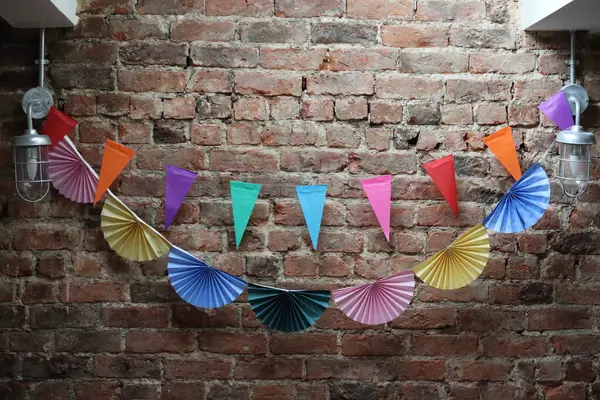 Açığa çıkmış tuğla bir duvarda üçgen ve fan şeklinde süslemeleri olan canlı bir kağıt çelenk. Şenlikli ve yaratıcı bir iç dekorasyon sahnesi. Yüksek kaliteli fotoğraf.