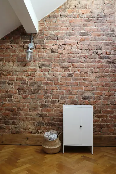 Bu iç mekan kırmızı tuğladan bir duvar, endüstriyel bir asma ışık, minimalist beyaz bir dolap ve yuvarlanmış atımlarla dolu dokuma bir sepet içeriyor, rahat ve çağdaş bir atmosfer yaratıyor..