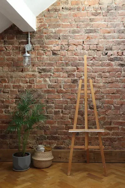 Kırmızı tuğlalı bir duvar, asılı bir ışık, ahşap bir sehpa, bir bitki ve dokuma sepetli rahat bir sanat stüdyosu. Sanatla ilgili projeler, iç tasarım ilhamı veya arkaplan olarak ideal.