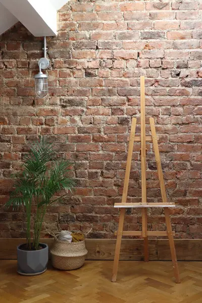 Kırmızı tuğlalı bir duvar, asılı bir ışık, ahşap bir sehpa, bir bitki ve dokuma sepetli rahat bir sanat stüdyosu. Sanatla ilgili projeler, iç tasarım ilhamı veya arkaplan olarak ideal.