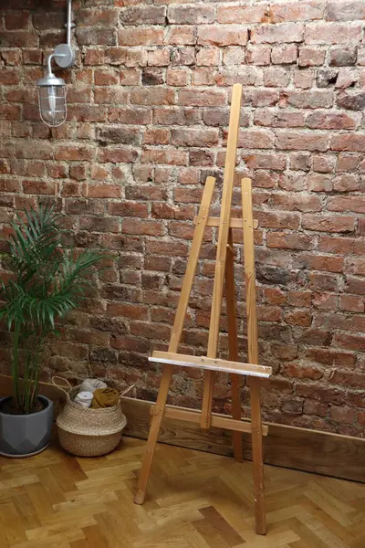 Kırmızı tuğlalı bir duvar, asılı bir ışık, ahşap bir sehpa, bir bitki ve dokuma sepetli rahat bir sanat stüdyosu. Sanatla ilgili projeler, iç tasarım ilhamı veya arkaplan olarak ideal.