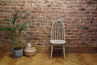 A beige wooden chair is placed against a textured exposed brick wall. The warm wood floor and the natural tones of the decor elements create a cosy, minimalist, and inviting interior setting. clipart