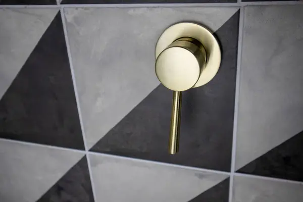 Geometrik siyah ve gri fayanslı duvara monte edilmiş modern bir altın duş kabzası. Yüksek kalite fotoğraf