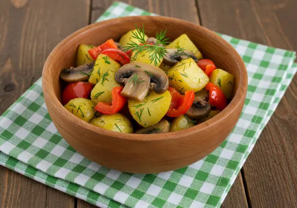 Lezzetli bir patates, mantar ve kırmızı biber salatası. Kırsal ahşap bir kasede ustalıkla hazırlanmış. Taze dereotuyla süslenmiş bu lezzetli yemek, yeşil ve beyaz kareli bir kumaş üzerinde sunuluyor. Hafif bir yemek ya da yan yemek kadar mükemmel..