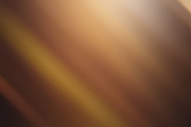 Yumuşak odaklı köşegen ışık çizgileri ile sıcak, altın-kahverengi soyut bir arka plan, zarif ve davetkar bir atmosfer yaratıyor..