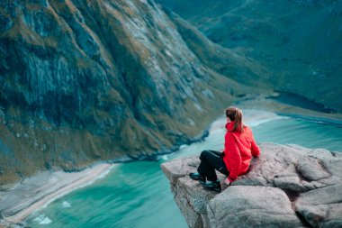 Maceracı kız dağın tepesinde oturuyor ve Kvalvika sahilindeki Ryten 'ın güzel manzarasının tadını çıkarıyor. Güzel Doğa Norveç Doğal Arazisi