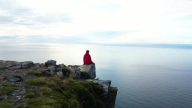 Dağın tepesinde oturan kırmızı ceketli kız güzel Norveç denizi manzaralı, Ryten, Lofoten adaları
