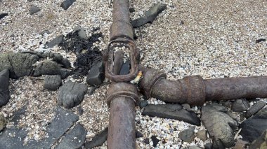 Rusty old metal pipe joint on the beach. Environmental decay.  clipart