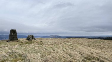Bulutlu, kasvetli bir günde otlaklarla ve uzun çam ağaçlarıyla dolu bir İskoç kırsalında yuvarlanıyor. Dağlar ve vadiler