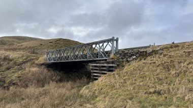 İskoç dağlarındaki bir yangının üzerindeki paslı eski metal köprü kışın karla kaplı. İskoçya 'da açık havada yuvarlanan tepeler. Güzel kırsal kesimde vahşi doğa manzarası