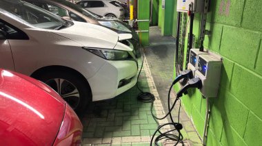 Karanlık bir yeraltı otoparkında elektrikli arabalar şarj oluyor. Şehirli grunge modern yaşam. Huysuz beton bina. Park etmiş arabalar. Sütunlar. Yol. Endüstriyel vahşi modernizm.