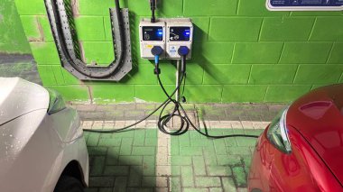 Karanlık bir yeraltı otoparkında elektrikli arabalar şarj oluyor. Şehirli grunge modern yaşam. Huysuz beton bina. Park etmiş arabalar. Sütunlar. Yol. Endüstriyel vahşi modernizm.