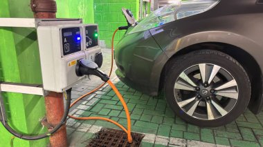 Karanlık bir yeraltı otoparkında elektrikli arabalar şarj oluyor. Şehirli grunge modern yaşam. Huysuz beton bina. Park etmiş arabalar. Sütunlar. Yol. Endüstriyel vahşi modernizm.