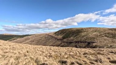 Glen Devon 'da Perthshire' daki Loch Tarret Barajı 'nın yanında yürüyorum. İskoç kırları ve tepeleri. Dağ sırası. Otlaklar, koyunlar ve akan su. İskoçya İskoç nehri aydınlık güneşli bir günde vahşi yerleri yakar.