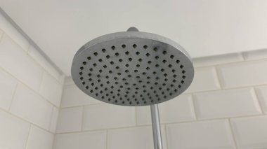 Havalı krom duş başlığı üstteki banyoda şık, beyaz fayanslı bir banyoya sığıyor.