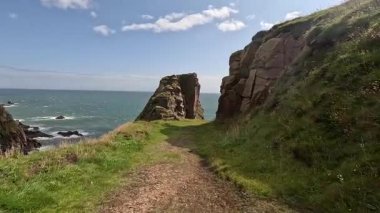 Buchan Bullers uçurumun kenarında yürüyor. Güzel İskoç engebeli kıyı şeridi Kuzey Denizi yamacı yaz güneşinin altında