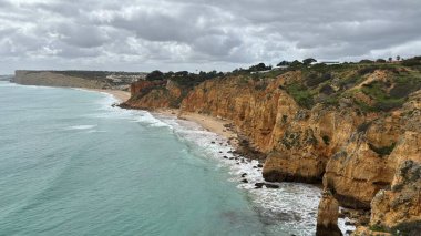 Lagos yakınlarındaki çarpıcı Algarve kıyı şeridi dramatik uçurumlar, altın plajlar, turkuaz sular ve parlak bir gökyüzü altında manzaralı okyanus manzarası.