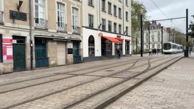 Nantes kentsel caddelerinde faaliyet gösteren modern Fransız yolcu tramvaylarının sokak seviyesindeki görüntüsü günlük hareketle toplu taşımayı gösteriyor.