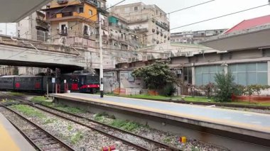 İtalyan yolcu trenleri istasyonlarda ve Napoli 'deki raylar boyunca hareket halinde, güneydeki bir şehir merkezinde toplu taşıma ve demiryolu ulaşımını yakalıyor.