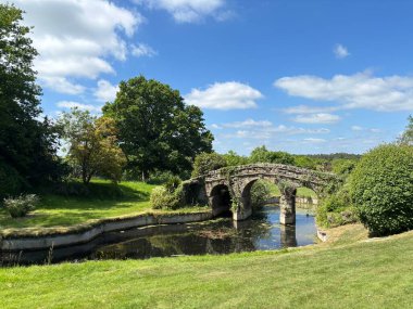Yazın, ördek havuzu, taş köprü, yeşil çimen ve yapraklı ağaçlar, huzurlu kırsal cazibe ve geleneksel manzara güzelliği olan İngiliz kır bahçesi..