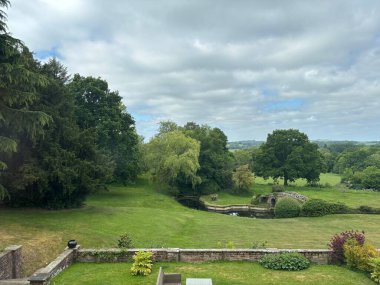 Yazın, ördek havuzu, taş köprü, yeşil çimen ve yapraklı ağaçlar, huzurlu kırsal cazibe ve geleneksel manzara güzelliği olan İngiliz kır bahçesi..