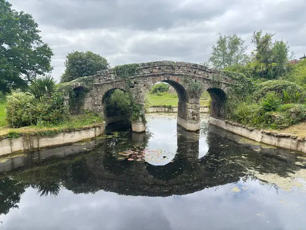 Yazın, ördek havuzu, taş köprü, yeşil çimen ve yapraklı ağaçlar, huzurlu kırsal cazibe ve geleneksel manzara güzelliği olan İngiliz kır bahçesi..