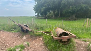 Rusty abandoned farm rollers resting in overgrown grass, showing weathered metal and rural decay in the Scottish countryside.