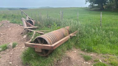 Rusty abandoned farm rollers resting in overgrown grass, showing weathered metal and rural decay in the Scottish countryside.