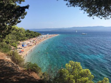 Zlatni Rats 'in ikonik çakıl taşı sütyen üzerine çam ağaçları ve Bols Akdeniz mimarisi tarafından desteklenen hava görüntüleriyle yansıtılıyor..