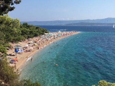 Zlatni Rats 'in ikonik çakıl taşı sütyen üzerine çam ağaçları ve Bols Akdeniz mimarisi tarafından desteklenen hava görüntüleriyle yansıtılıyor..